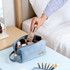 A flannel cosmetic bag in blue, filled with various beauty products, sits on a table beside a bed.