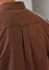 A brown patterned long sleeve shirt featuring a back pleat and a collar, with a logo on the garment.