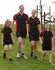 A group of four people wearing matching black and red Men's Alliance polo shirts and shorts, walking on grass.