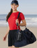 A woman in a red shirt and black shorts carries a navy blue duffle bag with a drink bottle visible in the side pocket.