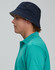 A contrasting underbrim bucket hat in navy, worn by a person in a teal polo shirt, featuring ventilation eyelets.
