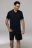 A man wearing a dark navy polo shirt with contrasting green accents, paired with black shorts. The shirt features a logo.