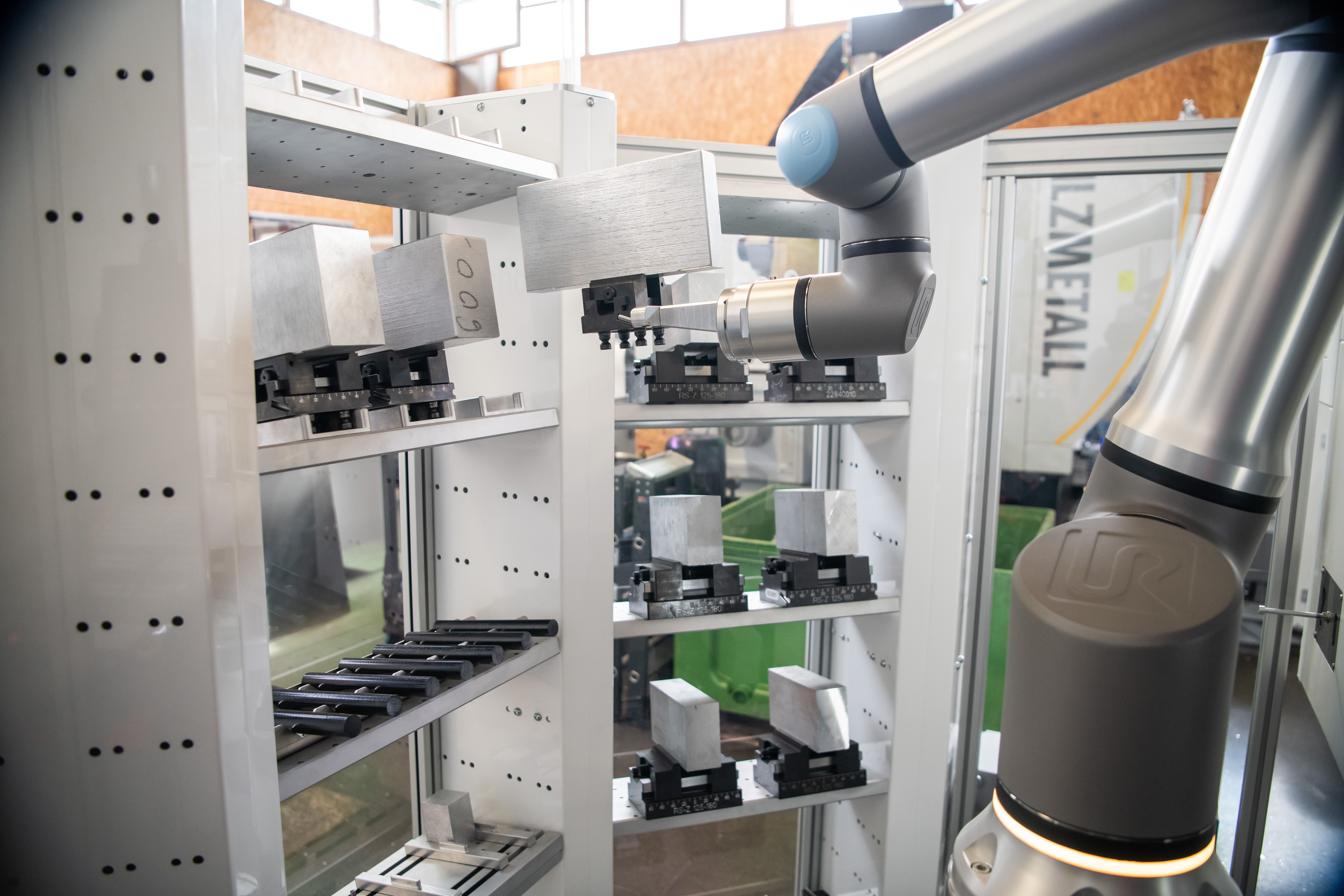 Universal Robots cobot arm picking precision machined aluminum workpieces from a multi-shelf parts rack at LZMetall &mdash; automated machine tending cell