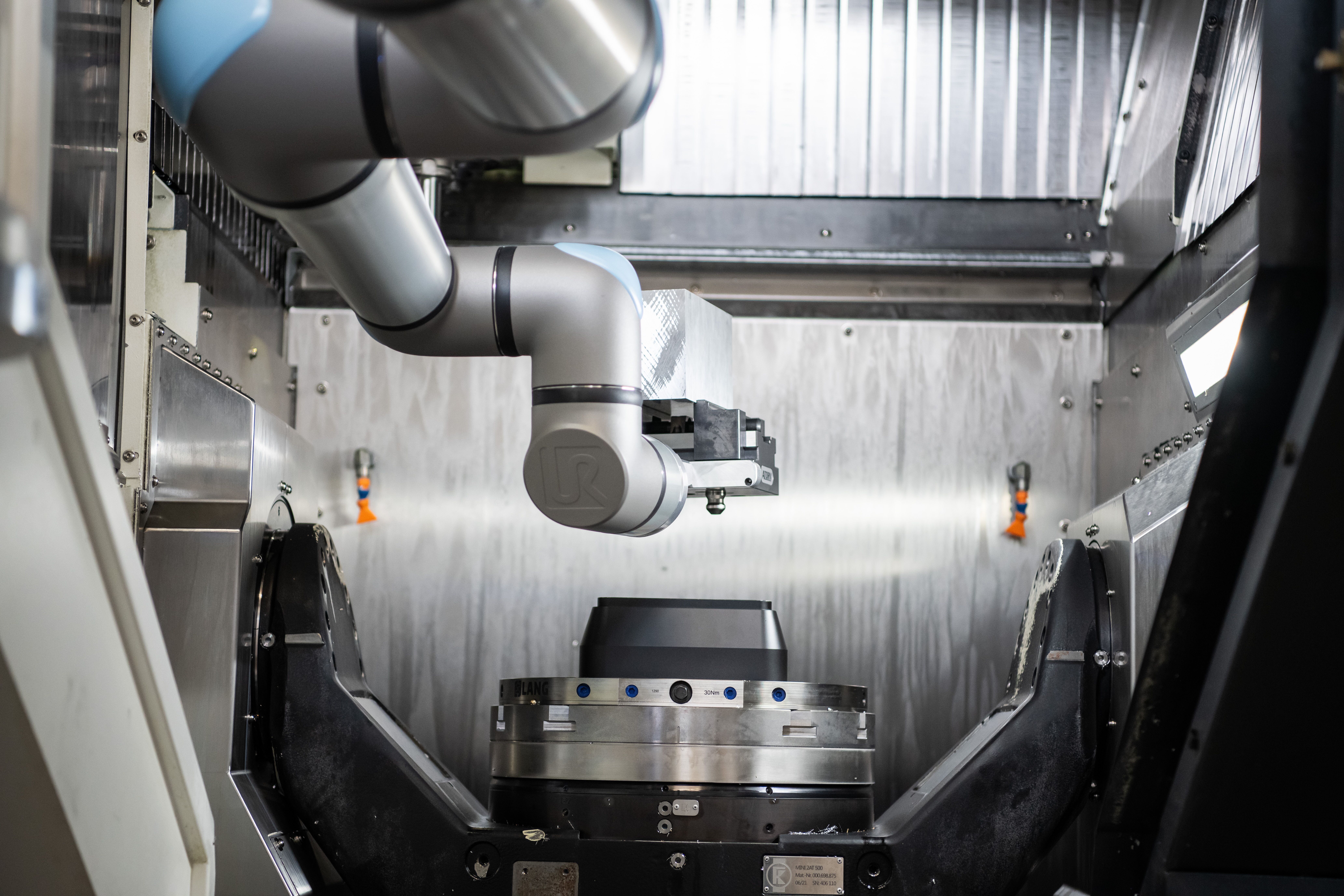 Universal Robots cobot arm reaching inside CNC machining center enclosure to load a large precision-machined disc component onto the chuck at Endutec