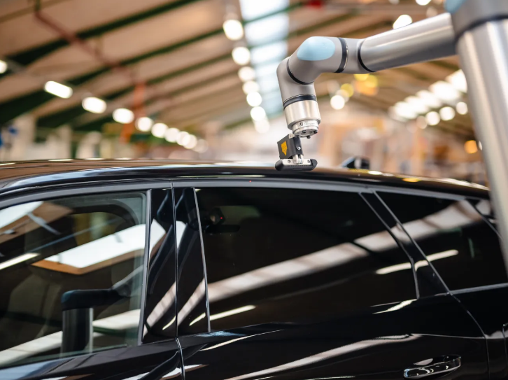 Universal Robots UR8 Long cobot arm performing quality inspection or seam sealing on a black automotive vehicle body &mdash; automotive assembly plant environment