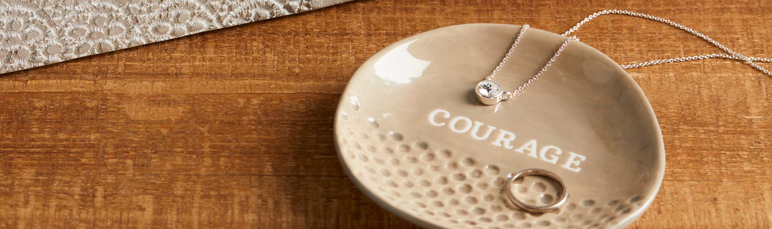 A photo of a jewelry keeper plate with the word courage printed on it and a ring laying inside