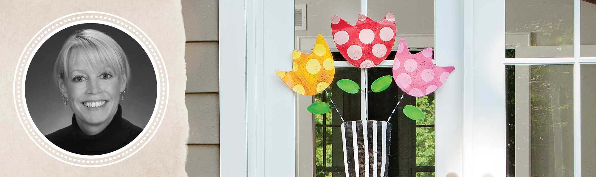 Peri's photo next to her work screened flowers hanging on a white and glass door