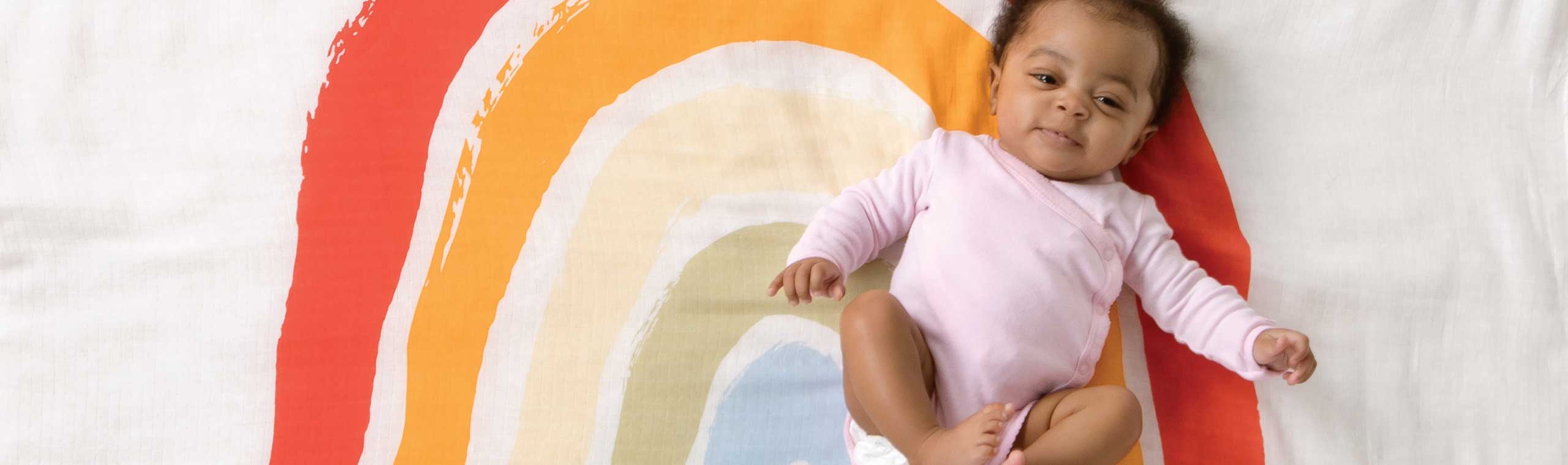 a baby girl laying on top of a rainbow blanket