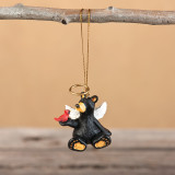 Hanging from a branch black bear figurine ornament - the bear has white wings and a red bird on one shoulder