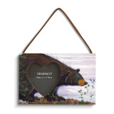 A rectangular wood hanging frame with a 2x2 inch heart shaped photo opening and has a painted image of a black bear sniffing huckleberries.