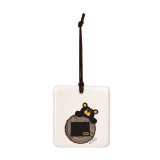 A white square hanging ornament with a black bear peeking over a tree stump with Colorado on it.