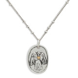 Close up view of the pendant on a silver necklace with a silver oval shaped pendant with the image of an angel holding a gold heart.