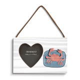 A rectangular hanging white wood frame ornament with a graphic red crab on a blue background with a 2x2 heart shaped opening for a photo.