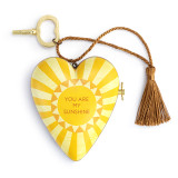 A heart shaped musical sculpture in a yellow sun pattern that reads "You Are My Sunshine". The heart has a bronze tassel and gold key attached.