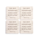 A set of four cream square ceramic coasters that say "The Best Adventures Don't Come With A Map" with the hundred acre lightly in the background.