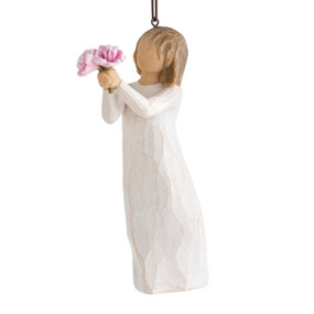 Front view of female figure in cream dress holding out small bouquet of pink peonies, ornament loop affixed to top of head