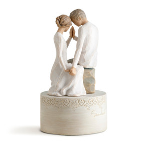 Couple figures sitting across from each other touching heads and hands on cream cylindrical stand carved with hearts