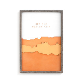 A gray frame enclosing an orange canyon wall art piece that reads "off the beaten path".