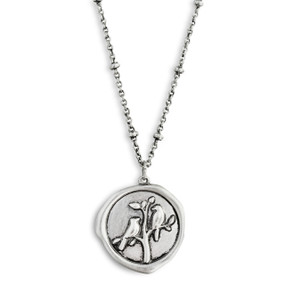 A close up image of a circular pendant with two birds sitting on a tree on a dainty silver necklace.