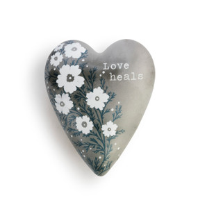 A gray heart shaped keeper that says "Love heals" is decorated with white flowers and displayed on a white background.