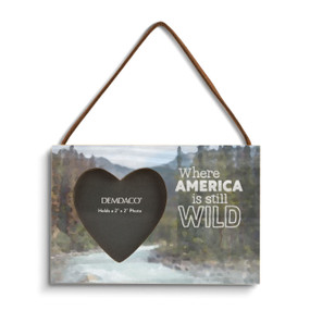 A rectangular wood hanging ornament with a 2 inch heart shaped opening for a photo next to the saying "Where America is still Wild" on a mountain stream background.