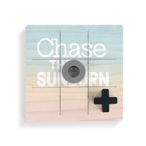 A square wood board for tic tac toe in sunset colors that says "Chase the Sunburn" with a gray O and black X piece on top.