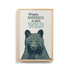 A graphic canvas print of a bear's head with the saying "Where America is still Wild" above it, in a light wood frame.