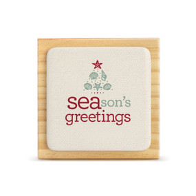 A light wood square plaque with a bone tile attached that says "SEAson's greetings" with the image of a tree made of seashells.