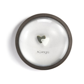 A round paperweight with a wood frame and the image of a white and black heart shaped stones that says "always".