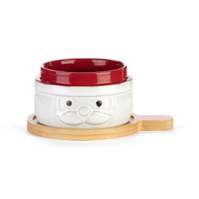 A red and cream ceramic bowl with Santa's face sitting on a round light wood board with a short handle.