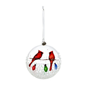 A clear glass ball ornament with an image of two cardinals sitting on a holiday string of lights.