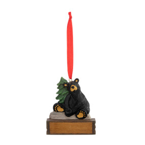 An ornament of a black bear sitting on a stone next to an evergreen tree, hanging from a red ribbon. There is a spot in front for customization.