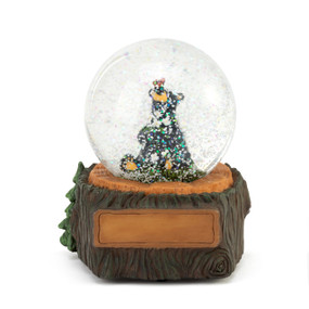 A musical snow globe with a black bear figurine holding white flowers sitting inside. The base looks like a wood tree stump with a place for customization.