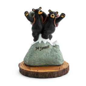 A figurine of two black bears wearing backpacks on the top of a snowy mountain that says "The Summit", on a base that looks like a wood stump.