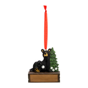 A hanging ornament with a black bear sitting by a pine tree on a rectangular base that can be personalized.