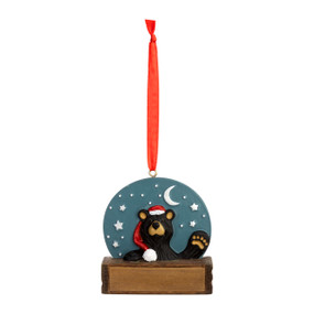 A hanging ornament with a black bear in a Santa hat in front of a blue sky with stars on a rectangular base that can be personalized.