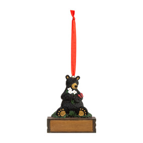 A hanging ornament of a black bear holding white flowers with a red butterfly on its arm sitting on a rectangular base that can be personalized.