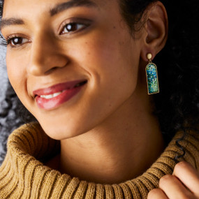 A woman wearing a pair of earrings with a vertical rectangle of blue and white artwork.