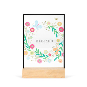 A large rectangular suncatcher in a light wood base. The image is a colorful floral illustration, and it says "Blessed" in the center.