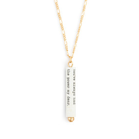 A gold chain necklace with a white scroll charm. The scroll has a saying from The Wizard of Oz.