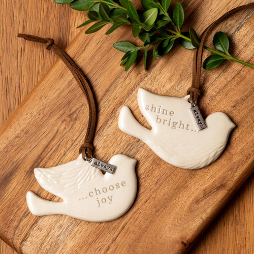 Set of two cream ceramic bird shaped ornaments. One says "choose joy" and the other says "shine bright". Each has a brown leather hanger and a metal tag that says "always".