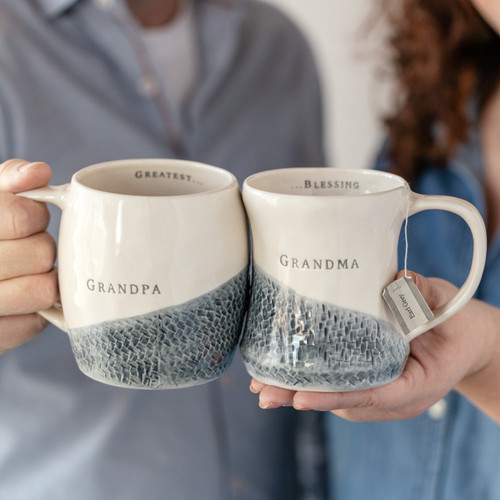 a woman and a man holding cream cermic mugs with blue detailing that read 'grandma' and 'grandpa' on the outside and 'greatest…' and '...blessing' on the inside rim