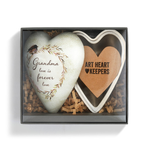 A beige art heart with a tan wreath holding a bird, white polka dots, and reads "Grandma love is forever love". Placed inside a black box with tan crinkle paper and a cardboard heart.