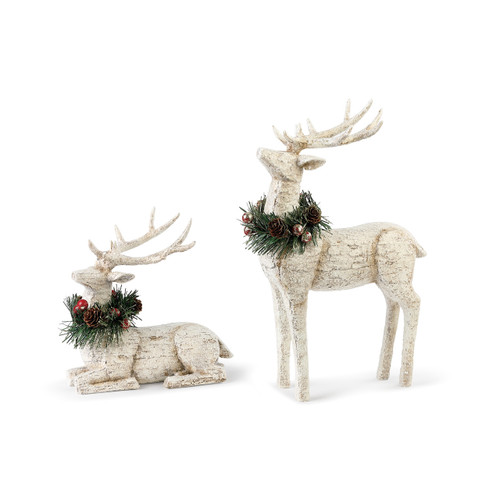 two decorative figures of white reindeer, one sitting and one standing, with wreaths around their neck