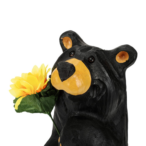 Detail view of the face on a tall black bear figurine holding a bright yellow sunflower.