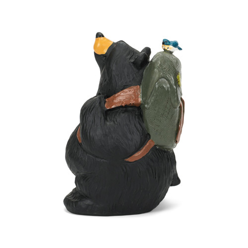 Left profile view of a black bear figurine wearing a green backpack with a little bluebird perched on top.