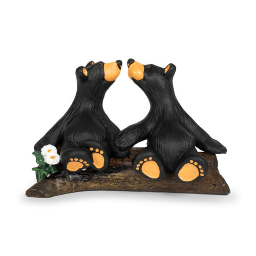 A figurine of two black bears sitting on a fallen log looking at each other with their noses almost touching.