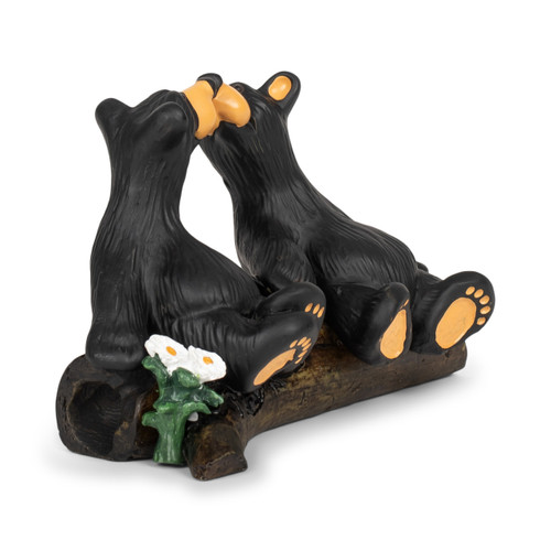 A figurine of two black bears sitting on a fallen log looking at each other with their noses almost touching, displayed angled to the right.