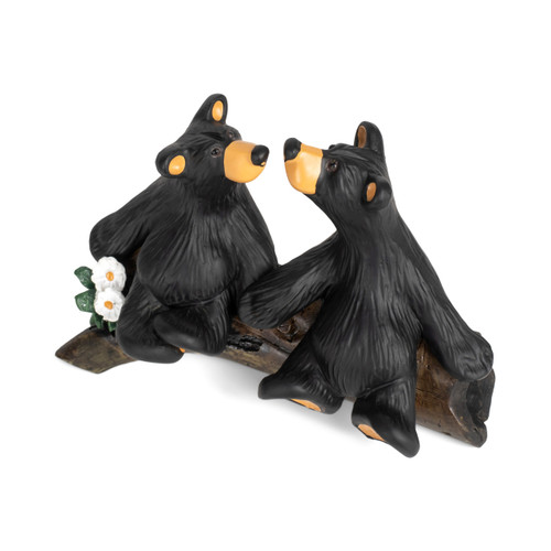 A figurine of two black bears sitting on a fallen log looking at each other with their noses almost touching, displayed angled to the left looking down.