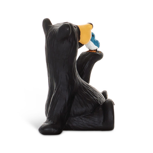 Right profile view of a small figurine of a black bear holding a small blue bird on its paw.